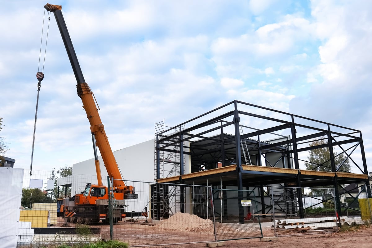 Truck crane operating at a fenced construction site with a new building structure