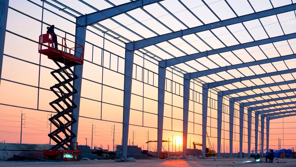 Welder on a scissor lift installing steel frame structures at sunset